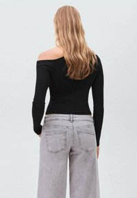 Schwarzes Oberteil mit schulterfreiem Schnitt und langen Ärmeln, kombiniert mit hellgrauen, weit geschnittenen Jeans. Das Oberteil hat eine taillierte Passform, und die Jeans verfügen über Gesäßtaschen.