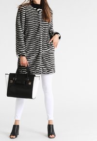 Cappotto in pelliccia sintetica con strisce zebra bianche e nere, abbinato a una borsa bicolore, jeans bianchi e mule nere con punta aperta.