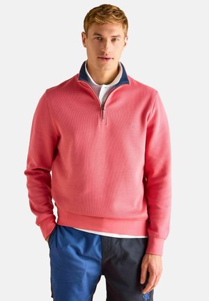 Coral quarter-zip sweatshirt with ribbed texture and a contrasting navy collar, paired with dark blue and black pants.