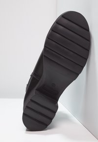 Czarna podeszwa buta z rowkowaną fakturą, wykonana z gumy. Charakteryzuje się płaskim designem z gładką krawędzią oraz wytłoczonym oznaczeniem rozmiaru na boku.