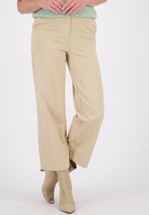 Beige wijde broek gemaakt van een soepele, rekbare stof, met strakke lijnen en subtiele stiksels, gecombineerd met lichtbeige enkellaarsjes.