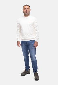 Camicia bianca a maniche lunghe con testo rosso, jeans blu e scarpe grigio scuro. Design semplice, tessuto morbido e vestibilità casual.