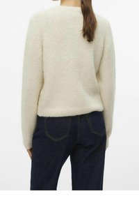 Elfenbeinfarbener Strickpullover mit einer weichen, strukturierten Oberfläche und einem lockeren Schnitt, kombiniert mit dunklen Jeans aus Denim mit Gesäßtaschen und subtilen Nähten.