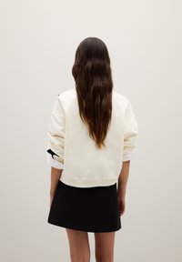 Felpa crema con maniche oversize, abbinata a una mini gonna nera. La felpa presenta un design corto e polsini bianchi sotto.