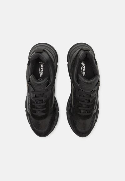 Black sneakers with a textured mesh and leather upper, rounded toe, multiple lace eyelets, and a side zip detail. Chunky sole design.