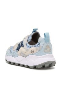 Zapatilla en azul claro y beige con texturas de gamuza y malla, recortes circulares y una suela blanca que presenta tachuelas de tracción grises.
