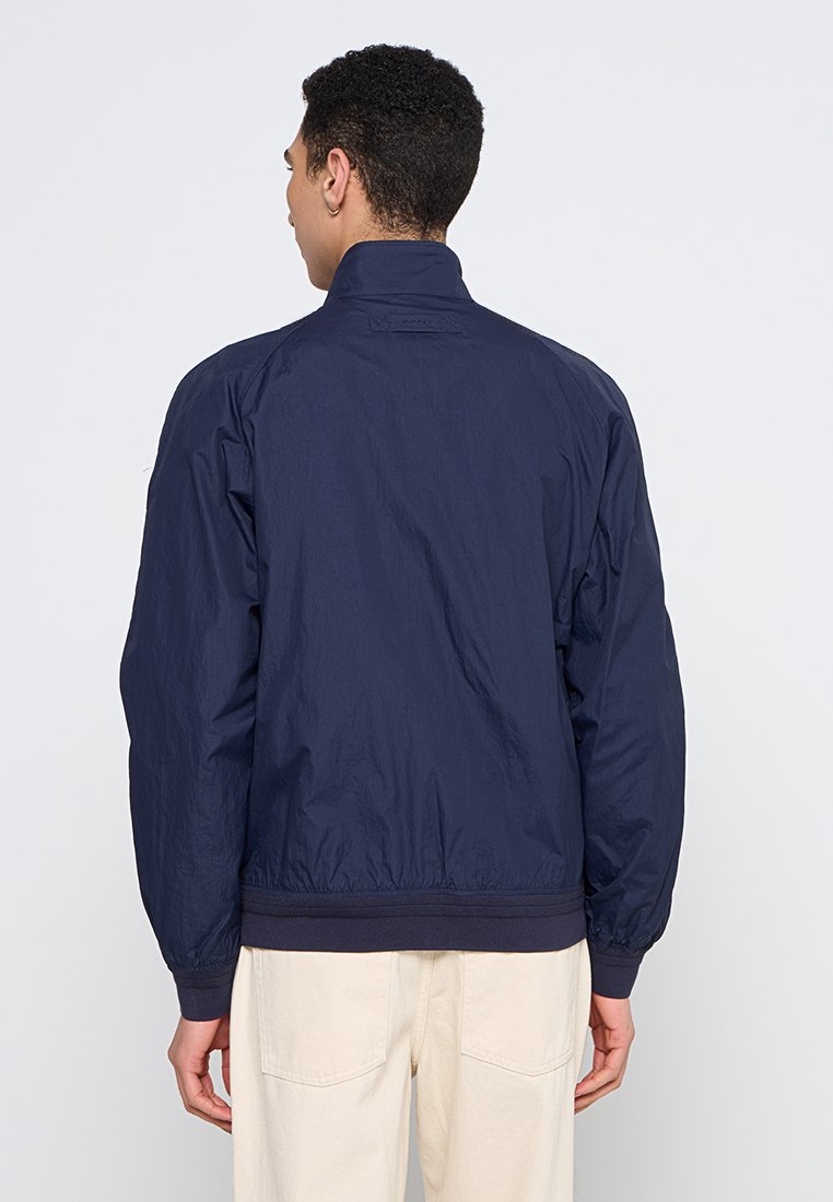 Marineblaues Windbreaker-Jackett, leichtes Material, elastische Bündchen und Saum, Stehkragen, mit einem dezenten Logo im Nackenbereich.