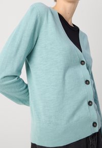 Light turquoise cardigan made of soft fabric, featuring a deep V-neck, long sleeves, and five dark buttons down the front.