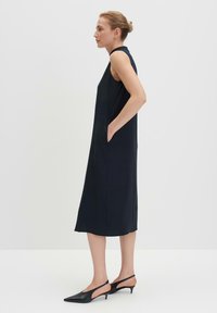 Navy-blaues ärmelloses Kleid mit geradem Schnitt und Seitentaschen. Der Stoff hat eine glatte Textur, kombiniert mit schwarzen spitzen Slingbacks.