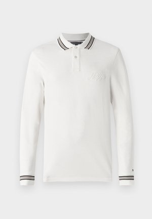 Camisa polo branca de mangas longas com uma pala de dois botões, colarinho às riscas em preto e branco, logótipo bordado no peito e punhos às riscas.