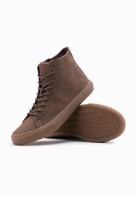 Zapatillas altas marrones hechas de cuero texturizado, con cordones a juego, un cuello acolchado y una suela de goma con un patrón de espiga.