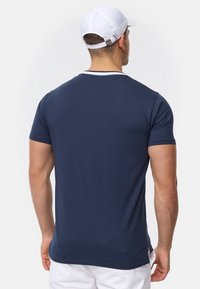Camiseta de manga corta azul marino, hecha de tela suave, con un cuello acanalado y aberturas laterales para mayor comodidad, combinada con pantalones cortos blancos.