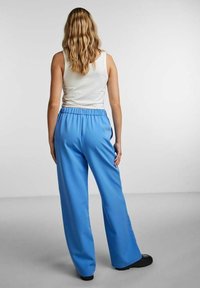 Ljusblå vida byxor med elastisk midja, kombinerat med en figursydd vit tanktopp. Slät textur, inga synliga mönster eller detaljer.