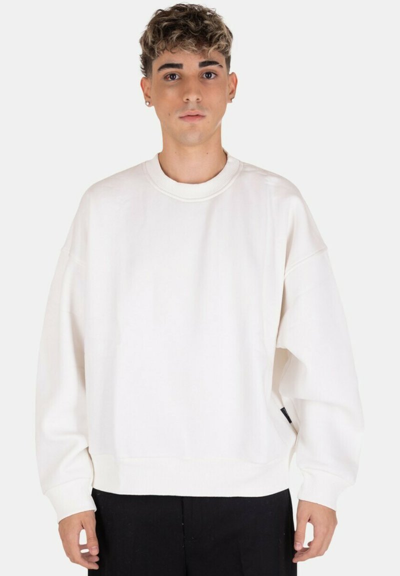 Felpa bianca oversize con collo rotondo, polsini e orlo a coste. Realizzata in tessuto morbido, presenta un'etichetta laterale discreta. Design semplice e moderno.
