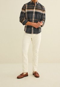 Koszula w kratę z button-up w ciemnych odcieniach, z pomarańczowymi i kremowymi paskami, zestawiona z białymi spodniami i brązowymi loafersami. Posiada klasyczny kołnierz i kieszeń.
