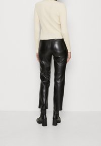 Pantalones de cuero sintético negros con corte ajustado, cintura alta, bolsillos traseros y detalles de costura sutiles. Combinados con un suéter de punto crema.