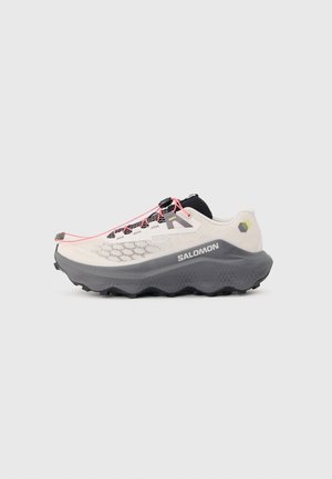 Light beige and black Salomon trail running shoe with thick gray sole and neon pink quick-lace system, viewed from the side.