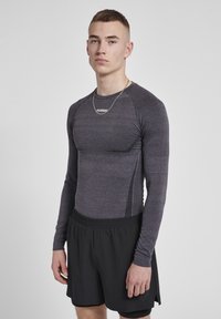 Langærmet, tætsiddende sports-top i mørkegrå med tekstureret materiale og kontrasterende sorte sidepaneler, parret med løse sorte shorts.