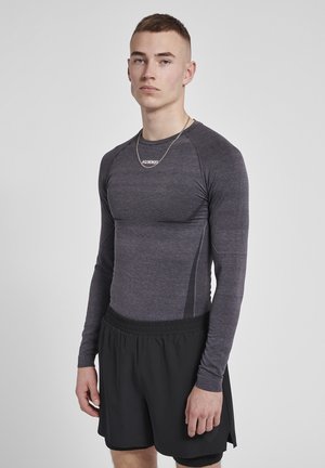 Langermige, getailleerde sporttop in donkergrijs met een gestructureerd materiaal en contrasterende zwarte zijpanelen, gecombineerd met losse zwarte shorts.