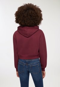 Krótkie bordowe bluzy z kapturem ze sznurkiem, wykonane z miękkiego materiału, zestawione z niebieskimi dżinsami o klasycznym kroju kieszeni.