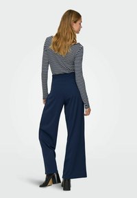 Navy wide-leg trousers paired with a fitted, striped long-sleeve top. The fabric appears smooth with a soft texture. Black heeled boots complete the look.
