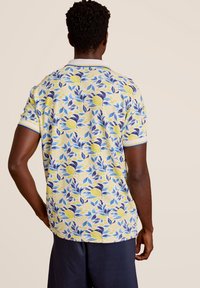 Korte mouw polo shirt met een gele basis, voorzien van een blauw en groen blad- en citroenprint, afgewerkt met een witte kraag en blauwe accentstrepen.