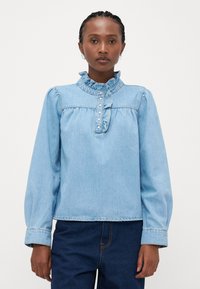 Αερόβια μπλούζα από ανοιχτό γαλάζιο τζιν με ριγέ κολάρο, κουμπιά μπροστά και μακριά μανίκια. Διαθέτει άνετη εφαρμογή και λεπτές ραφές.