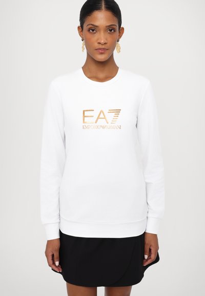 Bela mikica z dolgimi rokavi z metaliziranim zlatim logotipom "EA7 EMPORIO ARMANI". Gladka tekstura, okrogla ovratnica in rebrast rob.