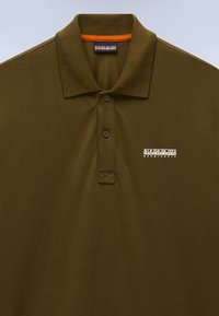 Polo de color verde oliva hecho de tela texturizada, con una tapeta de tres botones y un logo bordado en el pecho izquierdo. Cuello con detalle en naranja.