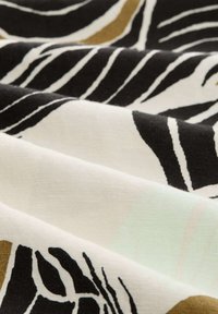 Tissu en coton avec une base blanche ; présente des motifs de feuilles noires et dorées. La texture semble lisse avec des plis drapés.