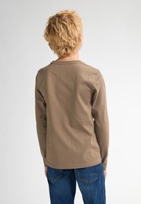 Camicia marrone in cotone a maniche lunghe con scollo rotondo e vestibilità rilassata, mostrata da dietro, abbinata a jeans blu.