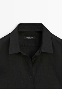 Zwart blouse met klassieke kraag, twee zichtbare knopen en een "Massimo Dutti"-label aan de binnenkant van de halslijn.