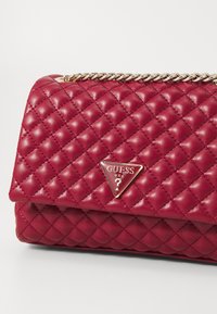 Borsa a tracolla in pelle trapuntata rossa con tracolla in catena dorata e distintivo a logo triangolare. Presenta una superficie texturizzata e un design elegante.