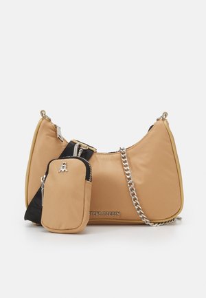 Beżowa torba na ramię z regulowanym czarnym paskiem, małą przymocowaną saszetką, srebrnym łańcuszkiem i logo Steve Madden na przodzie.