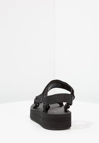 Black platform sandals with adjustable straps, textured footbed, and a sturdy rubber sole. Minimalist design with no additional accents.