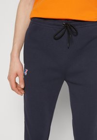 Marineblaue Sweatpants aus einem weichen Material mit einem elastischen Bund und schwarzem Kordelzug. Mit einem kleinen Logo auf dem Oberschenkel.