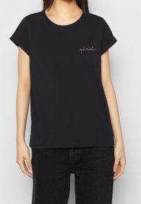 Svart bomullströja med rullade kortärmar och rund hals. Har rosa broderad text som står "optimistisk" på bröstet.