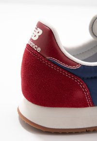 Baskets en daim rouge et tissu marine avec coutures blanches, talon renforcé, détail logo et semelle extérieure en caoutchouc léger.