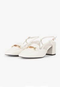 Zapatos slingback de cuero blanco con tacón cuadrado, punta afilada y detalle de cadena dorada en la parte frontal. Textura suave con correa en el tobillo.