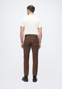 Καφέ καμπάνες κολομβιανής, με στενή εφαρμογή, που διαθέτουν δύο πίσω τσέπες και καθαρό σχέδιο ζώνης. Φοριούνται με λευκό πουκάμισο κοντό μανίκι.