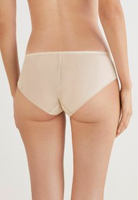 Mutande beige a vita alta realizzate in un tessuto liscio e elastico. Presentano un design senza cuciture e una cintura larga per un comfort aggiuntivo.