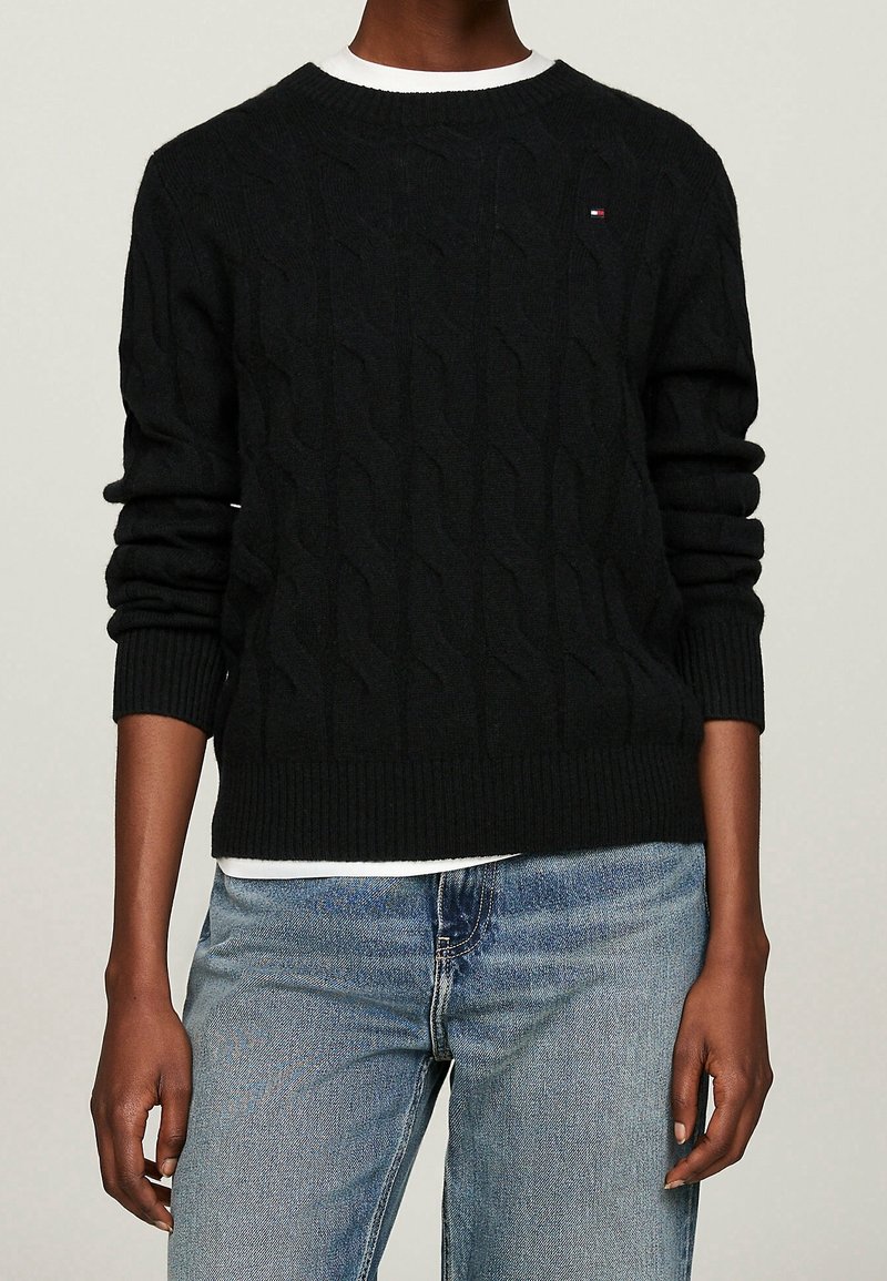 Maglione black a maglia con scollo rotondo e polsini e orlo a coste, abbinato a jeans azzurri chiari. Il maglione presenta motivi testurizzati.