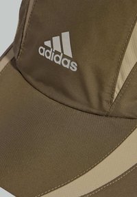 Hnědá čepice s bílým logem Adidas, doplněná kontrastními světle hnědými bočními akcenty a hladkou, texturovanou látkou. Kšilt je zakřivený.