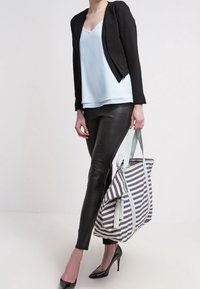 Blazer negro corto, camiseta de tirantes azul claro, leggings de cuero negros, tacones negros, llevando un bolso de mano a rayas con asas azul claro y borlas.