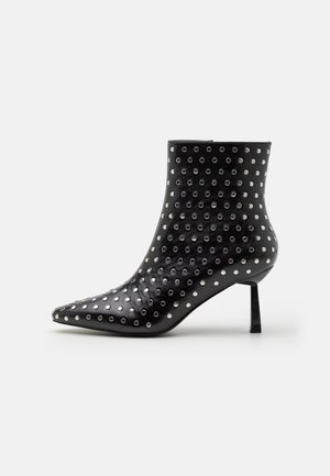 Zwarte leren enkellaars met een spitse neus, versierd met zilveren ringen en een slanke naaldhak. Gladde textuur en nauwsluitend ontwerp.