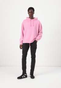Haut à capuche rose avec un cordon de serrage, tissu texturé, coupe décontractée ; associé à un jean noir et des baskets noires avec des accents blancs.