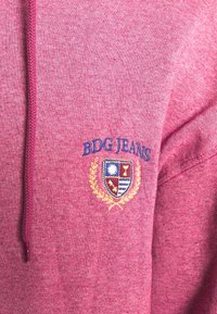 Bordeaux hoodie med en texturerad finish, med en broderad "BDG JEANS" logotyp och en färgad vapenskölddesign på bröstet.
