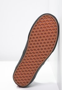 La semelle extérieure de la chaussure est en caoutchouc texturé avec un motif en losange, principalement noire avec une semelle inférieure en caoutchouc marron gomme.