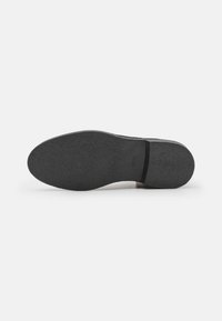 Semelle de chaussure en caoutchouc noir avec une surface texturée et un bord lisse, présentant un subtil logo de la marque embossé près de la zone du talon.