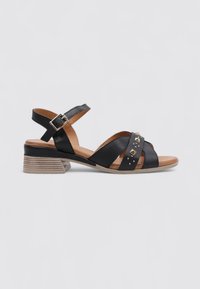 Sandales en cuir noir avec un petit talon carré, ornées de straps entrecroisées, de clous dorés et d'une sangle de cheville avec fermeture à boucle.